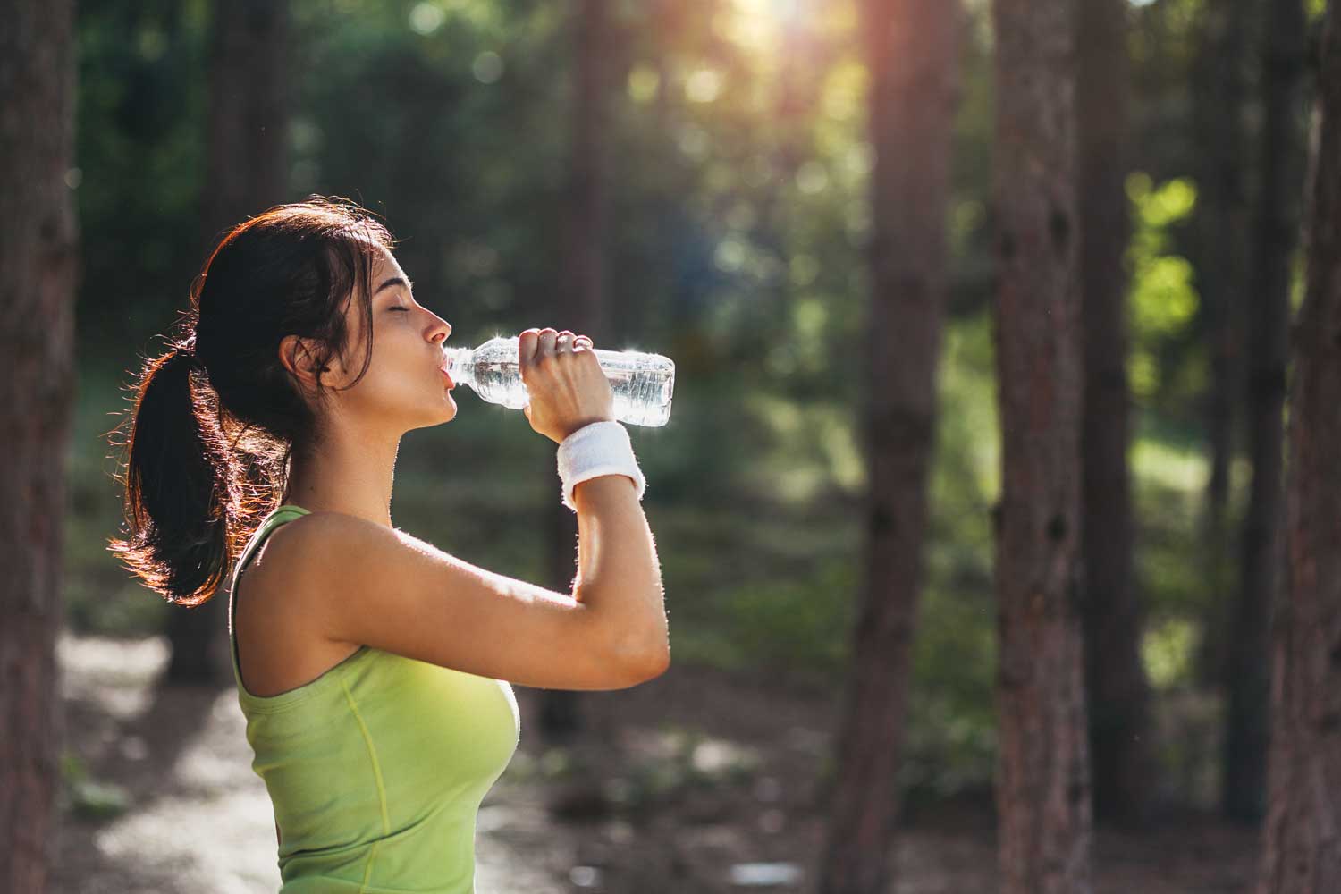 Woman who understands the health benefit of drinking water stopping to hydrate during a run | Spine & Sport Physical Therapy | San Diego, Irvine, Sacramento, CA