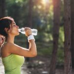 Woman who understands the health benefit of drinking water stopping to hydrate during a run | Spine & Sport Physical Therapy | San Diego, Irvine, Sacramento, CA